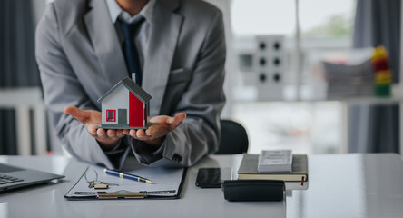 Male businessman or real estate agent holding house key for his client after signing contract in...