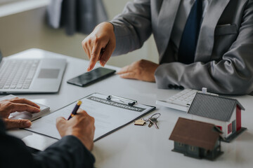 Businessman or real estate agent with house model laying down contract, having contract in place to...