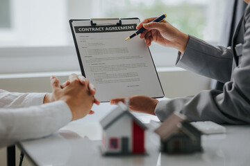 Businessman or real estate agent with house model laying down contract, having contract in place to...