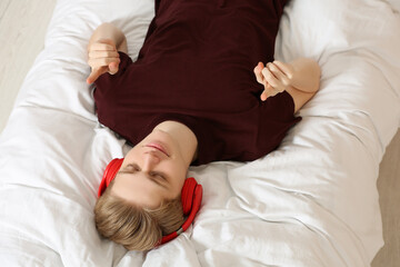Teenage boy listening to music with headphones on bed, above view
