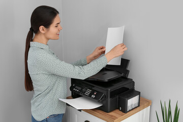 Woman using modern printer on chest of drawers at home