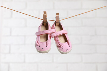 Cute pink baby shoes drying on washing line against white brick wall