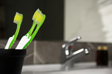 Light green toothbrushes in black toothbrush holder indoors, space for text