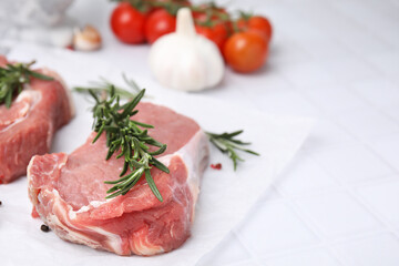 Fresh raw meat with rosemary on white tiled table, closeup. Space for text