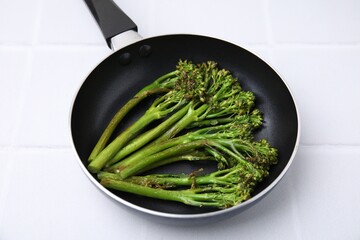 Frying pan with tasty cooked broccolini on white tiled table