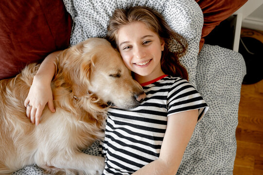 Pretty girl hugging golden retriever dog and lying in bed. Female teenager with purebred doggy pet labrador resting together