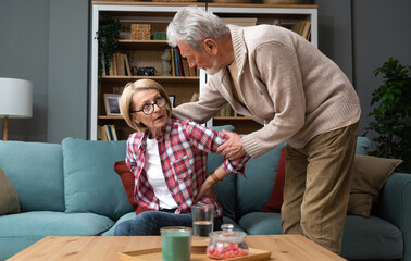 Portrait of senior couple in living room, Mature woman with pain in the shoulder. Upper arm pain, woman neck and shoulder pain and injury of back her husband massage her on sofa at home