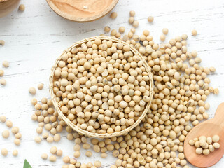Soybean or soya bean in a wooden spoon on white wooden background. Used as a base for making soy...