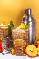 Iced peach tea, or peach lemonade with lime, mint,crushed ice and bar utensils 
on high-colored golden beige background 