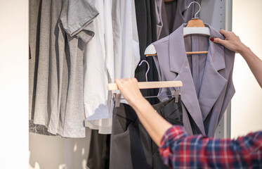 Female hand choosing clothes for checked pattern trousers on the rack in cloth shop at a department store. Check price, discount, and promotion of clothing products.