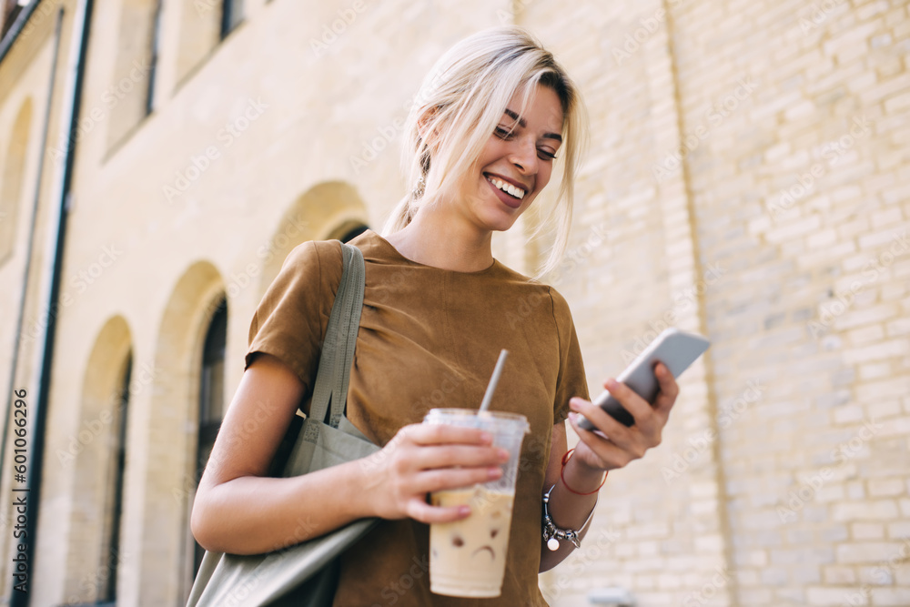 Poster cheerful travel blogger with ice coffee enjoying mobile chatting and messaging via cellular technolo