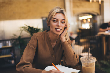 Caucasian female student looking at camera and studying coffee time in cafe interior, portrait of...