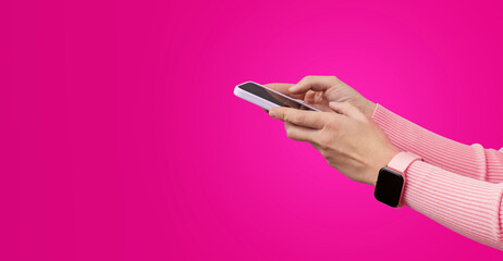 Woman holding sartphone and wearing smart watch against bright pink background