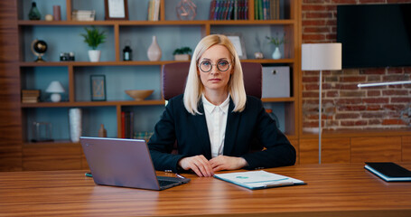 Fototapeta na wymiar Portrait of lovely concentrated adult blond businesswoman in formal wear which sitting in front of camera in modern office