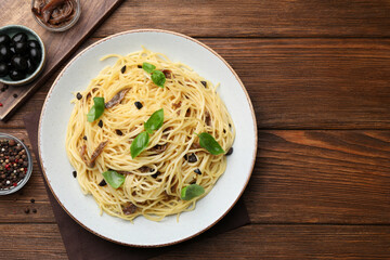 Delicious pasta with anchovies, olives and basil on wooden table, flat lay. Space for text
