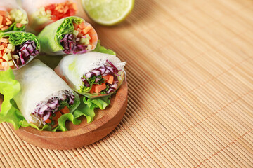 Tasty spring rolls wrapped in rice paper on bamboo mat, closeup. Space for text