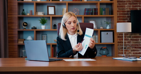 Fototapeta na wymiar Portrait of likable confident motivated experienced blond businesswoman in headset which holding online computer chat with colleagues and explaining financial report