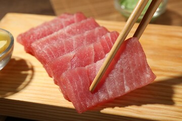 Taking tasty sashimi (piece of fresh raw tuna) from wooden board, closeup