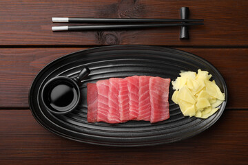 Tasty sashimi (pieces of fresh raw tuna) served with soy sauce and ginger slices on wooden table,...