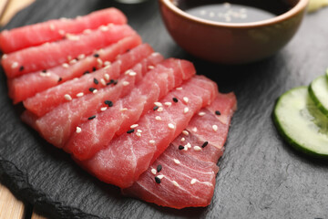 Fototapeta na wymiar Tasty sashimi (pieces of fresh raw tuna with sesame seeds) on black board, closeup