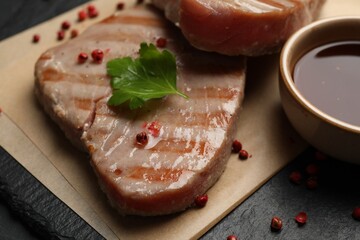 Delicious tuna steak with sauce, parsley and spices on board, closeup