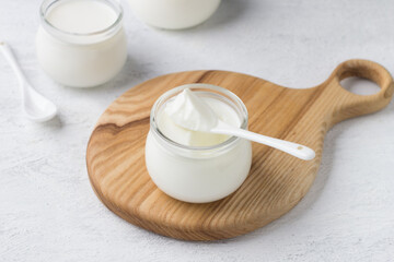 Fototapeta na wymiar Natural homemade yogurt in a glass jar on a wooden board on a light gray background
