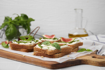 Tasty bruschetta with cream cheese, pesto sauce and fresh basil on wooden board
