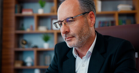 Attractive concentrated skilled hardworking bearded businessman in glasses sitting in front of laptop and typing on it during work in office,slow motion