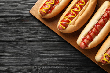 Delicious hot dogs with mustard and ketchup on black wooden table, top view. Space for text