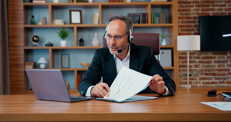 Business concept where likable motivated serious professional bearded ceo in headset discussing with business partners financial report using computer videocall