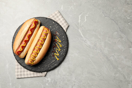 Delicious hot dogs with mustard and ketchup on light grey table, top view. Space for text