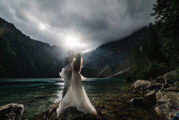 Romantic wedding couple in love standing on the stony shore of the Sea Eye lake in Poland. Scenic mountain view. The bride and groom. Morskie Oko. Tatra mountains. © Serhii