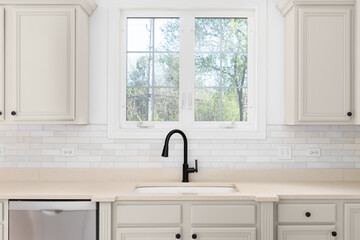 A black kitchen faucet detail with brown cabinets, tan countertop, and a marble subway tile...