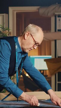 Vertical video Experienced tailor working in atelier to create new fashion collection, old couturier doing handmade luxury clothes in workshop. Small business owner creating custom made items.