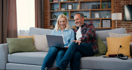 Attractive happy smiling married adult couple sitting on the sofa a t home and uses laptop to review their family photos,leisure concept