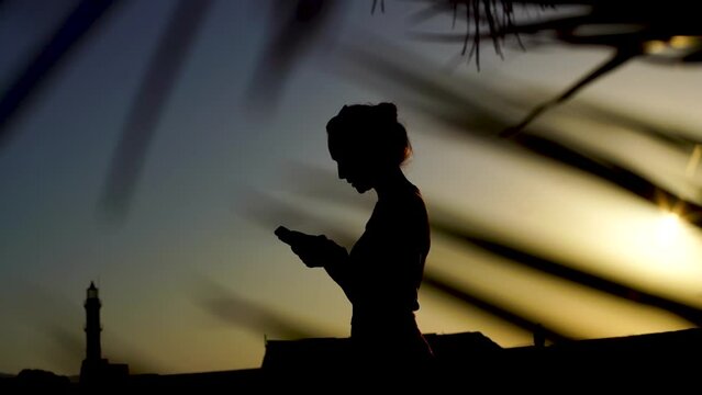 silhouette of a girl in palm trees at sunset. text messaging via phone