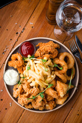 Snacks for beer: breaded squid rings, chicken nuggets, tempura shrimps, French fries, sauce and a glass of water.