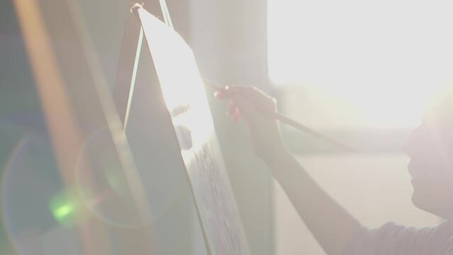 The artist is focused and attentive to the creation of her masterful works, which acquire life with help of her skillful hands and brushes. The sun shines through the window art workshop. At sunset