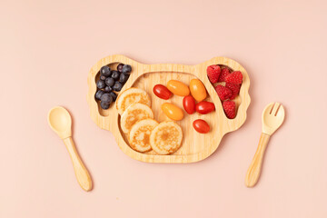 Top view of healthy breakfast for picky toddler with pancakes, tomatoes and berries. First safe plate and tableware for baby and toddler. Flat lay