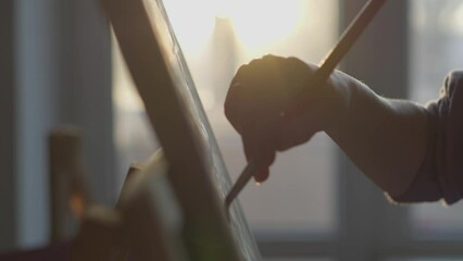 Silhouette of an artist painting with a brush at sunset. The artist's brush carefully draws on the easel, creating unique works of art from paints and brushes. Hobbies and creativity of young talent - Powered by Adobe