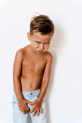 Cute little boy wearing blue jeans posing against white background with silly facial expression