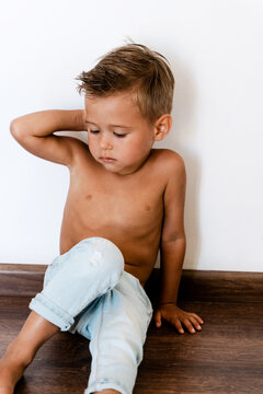 Cute little boy wearing blue jeans posing against white wall like fashion model