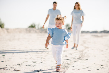 Baby closeup. Happy young family with a little daughter girl walking on the sand together outdoors. Mother, father, and child walk on the sandy beach. Family day and childhood concept.