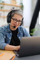 Technical customer support, a smiling mature woman in a headset works behind a laptop.