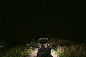View from the first person. Motorcycle steering wheel. On a tourist motorbike in the middle of a mountain dirt road. The night is dark, the stars are shining.