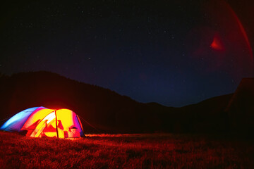 The tourist tent is illuminated by light. Starry sky. Tourism and active recreation. Overnight, camping in the Carpathian mountains, Ukraine. Copy space. - obrazy, fototapety, plakaty