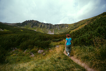 The back view of a female hiker with a leather hat, hiking to the top of Spytsi mountain, Carpathians, Ukraine. He has a long stick in his hands. Travel and active recreation.
