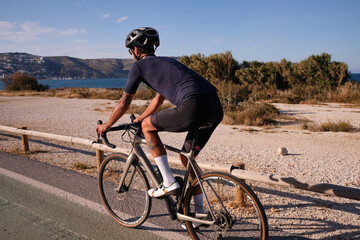 Professional male cyclist riding on bicycle near sea. Spanish cycling holiday. Motivational image. Triathlon concept. Xàbia, Alicante, Spain