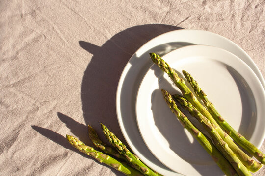Empty white plate, asparagus with contrast shadows on a gray background. Top of view. The concept of food in nature