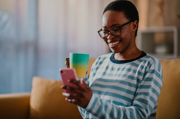 African american woman drinking coffee and using a smartphone at home
